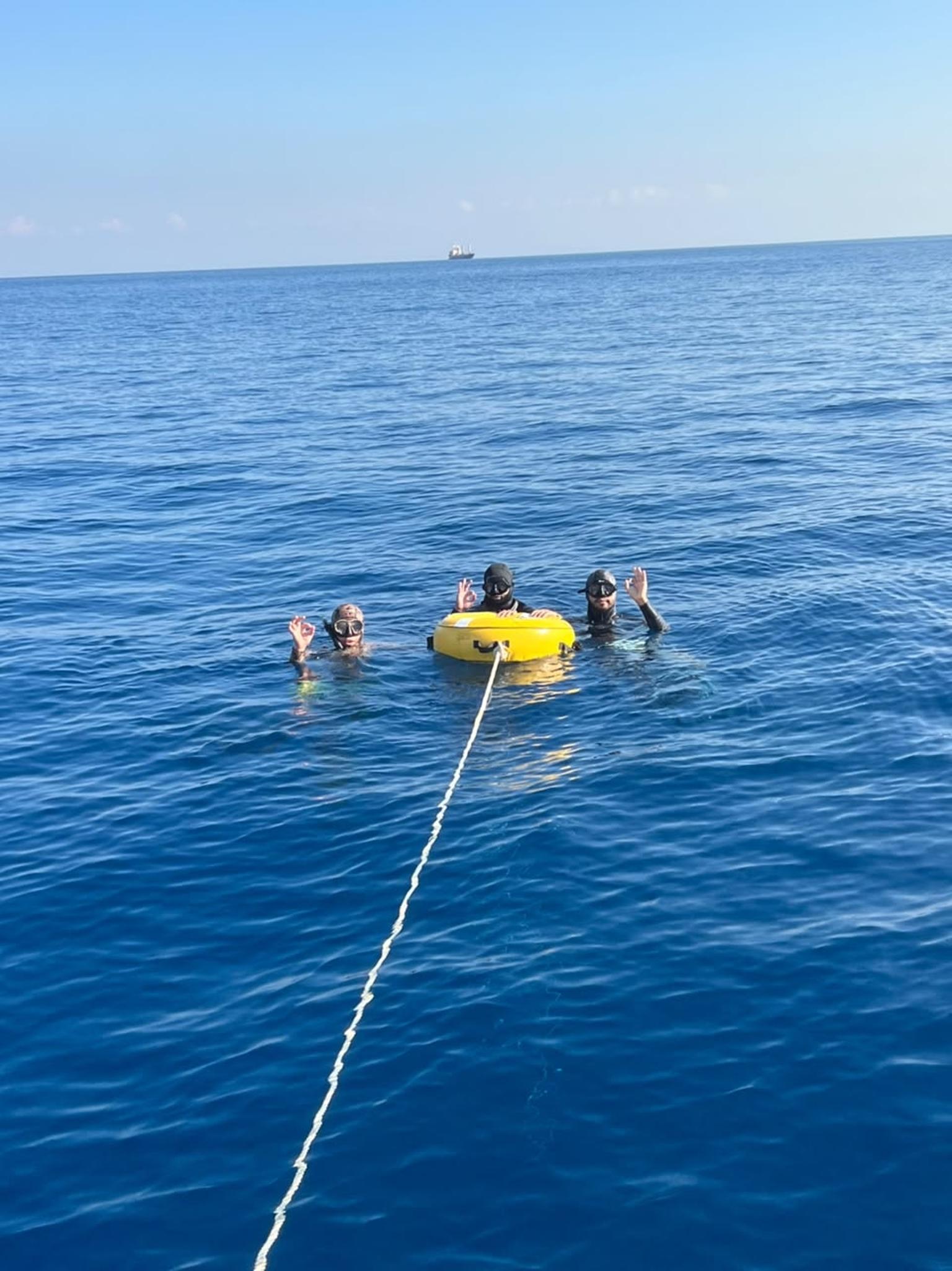 Three freedivers around a yellow buoy in open water