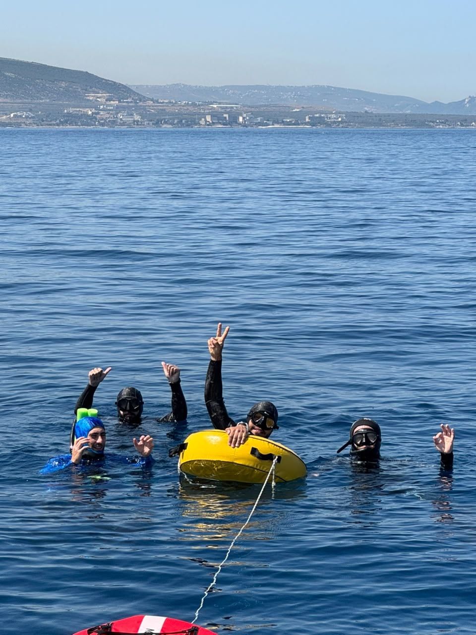 Freedivers waving from the water, the coast behind them