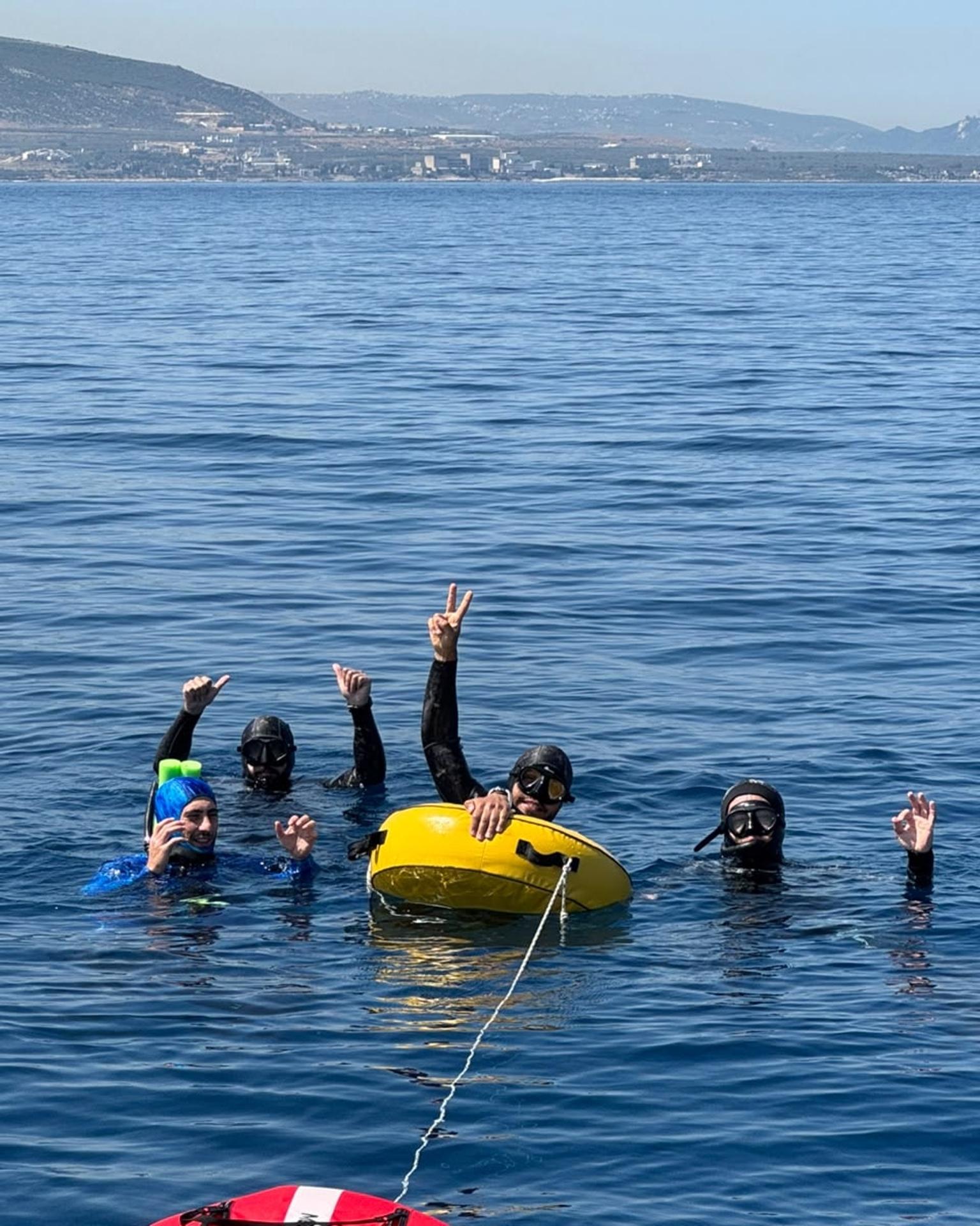 Freedivers waving from the water, the coast behind them