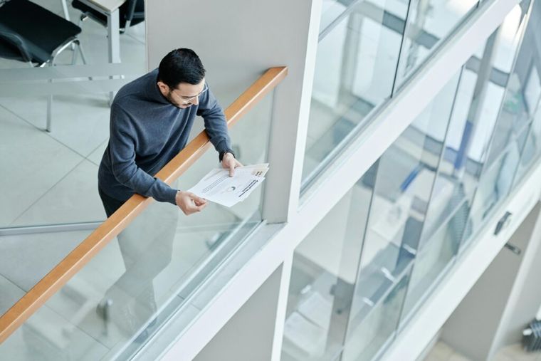 A man standing over a railing reading working papers.