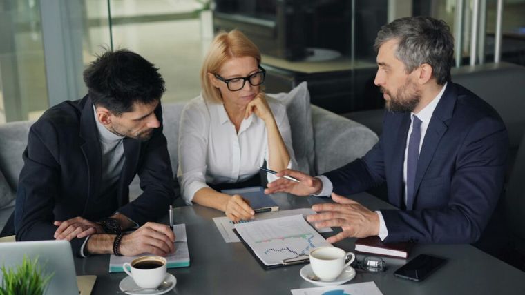Three business people sitting at a table with a laptop, representing strategic partnerships.