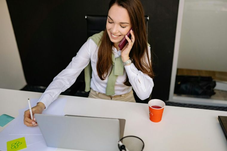 A woman engaged in a phone conversation, discussing retirement planning and financial advice, while seated at a desk with a laptop and notes.