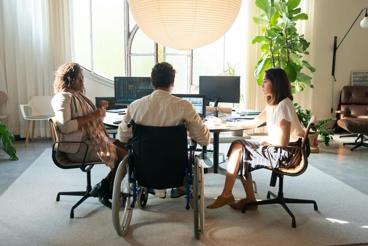 A group of coworkers holding a meeting with external monitors and stacks of tax documents to be filed.