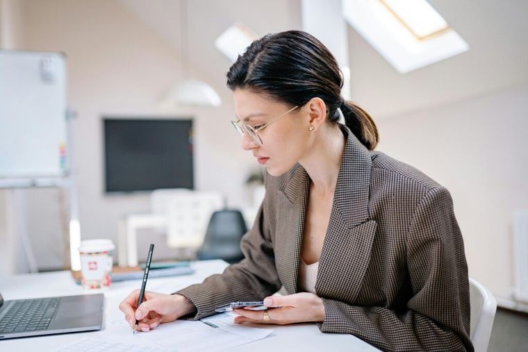 A woman in a brown coat writing notes, symbolizing retirement planning and preparation for SECURE 2.0 catch-up contributions and savings updates.