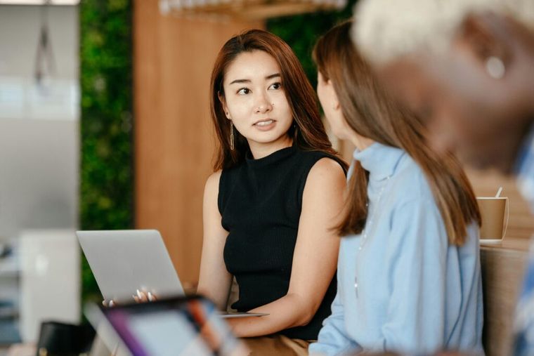 A professional woman seated at a wooden table in a modern workspace, reviewing documents with a colleague—suggesting collaborative business planning and thoughtful teamwork.