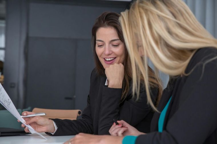 Two women smiling while discussing a paper.