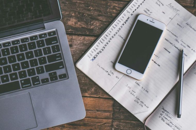 A rose gold iPhone displaying a digital checklist, placed beside a notebook and pen. The image represents organized financial planning—essential when strategizing to reduce or avoid the Net Investment Income Tax (NIIT)