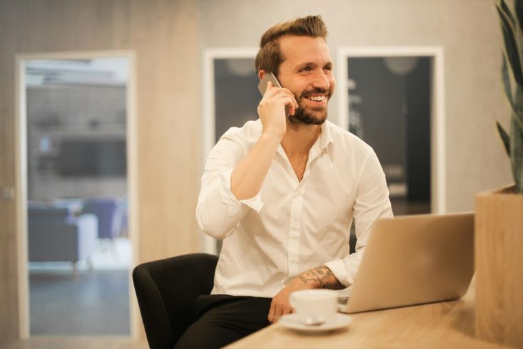 A man sits in a modern workspace using his smartphone, representing a founder staying informed and managing key financial strategies like QSBS to reduce capital gains taxes in 2025.