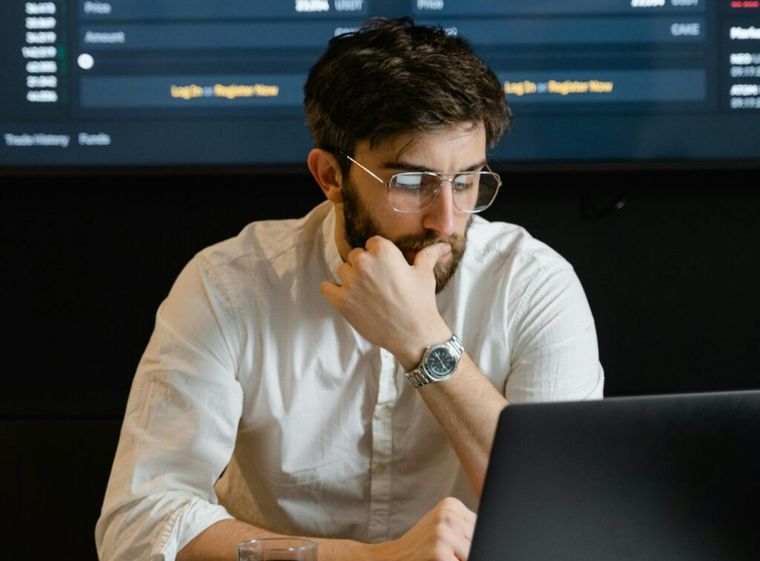 A thoughtful man in eyeglasses and a white dress shirt sits pensively in front of a laptop, considering how to reduce AI errors.