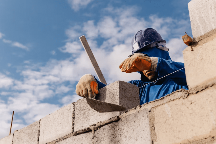 A construction worker laying a building block, representing the foundational steps of green building development and energy-efficient construction projects in 2025.