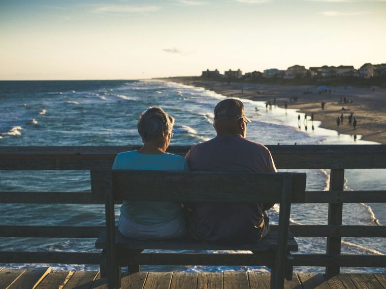 An older couple sitting peacefully on a bench by the ocean—symbolizing the long-term financial benefits of maximizing small business retirement contributions and securing future income.