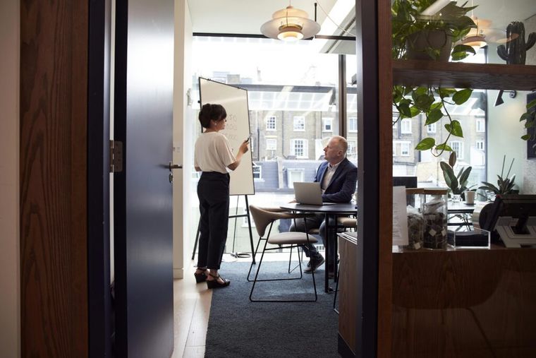 Professional woman standing beside a flip chart in a modern meeting room, delivering a presentation to colleagues.