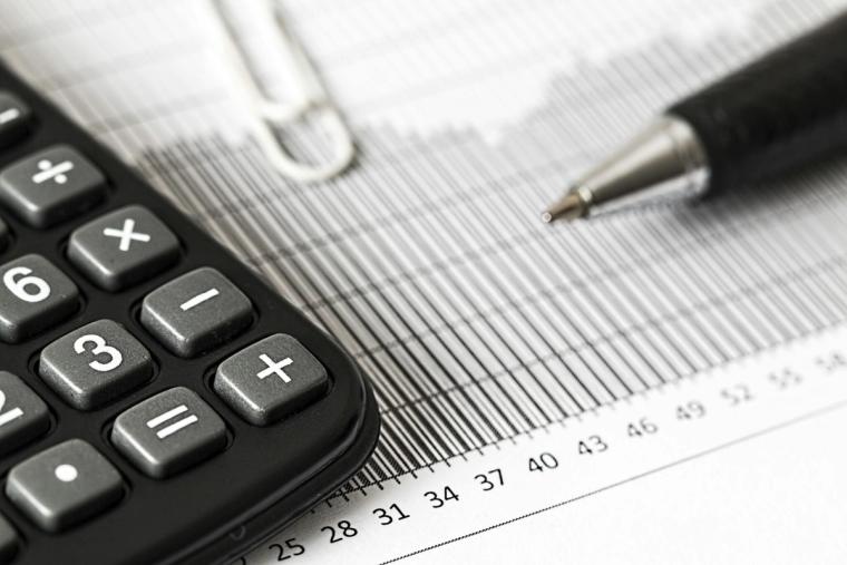Close-up of a calculator, pen, and paperclip placed on a financial chart with horizontal and vertical lines. The image emphasizes financial analysis, accounting, or data calculations.