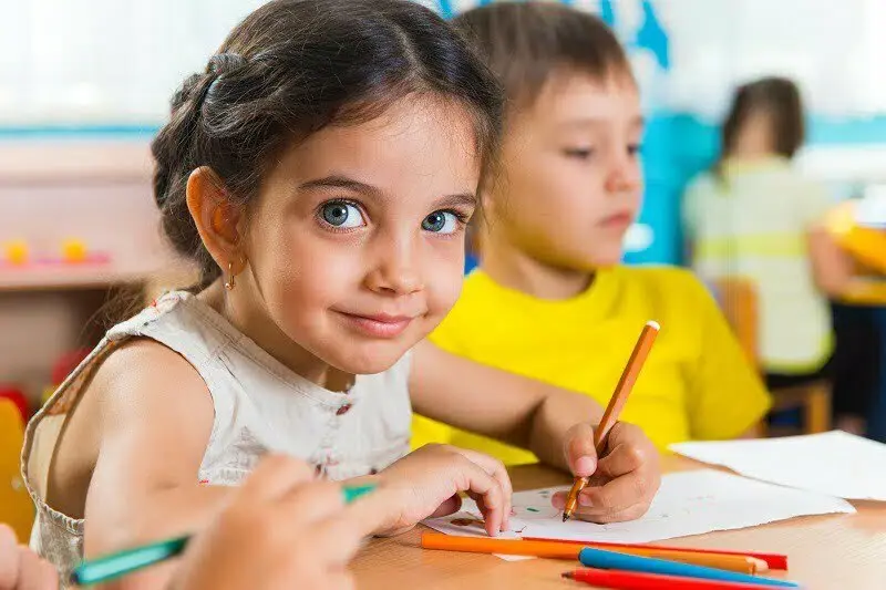 A young child in a white dress, sitting and drawing on a piece of paper