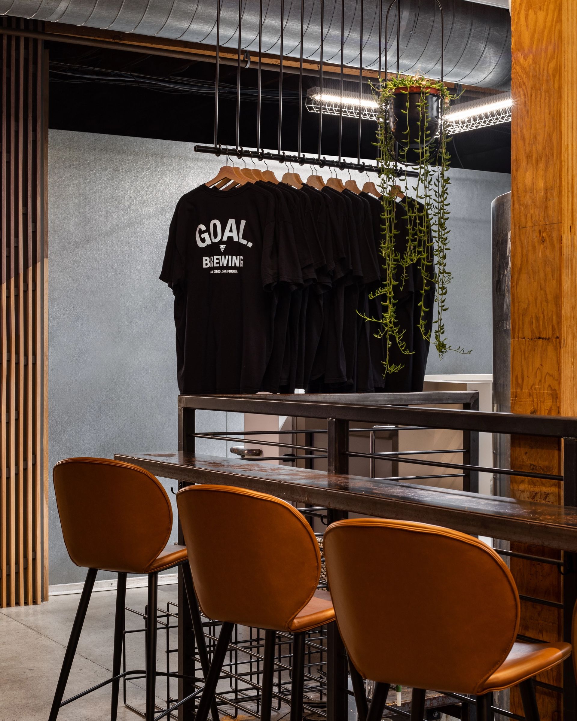 05 — Merch. A steel rail hangs the shirt inside the room: you don't have to leave the table to look at it.
