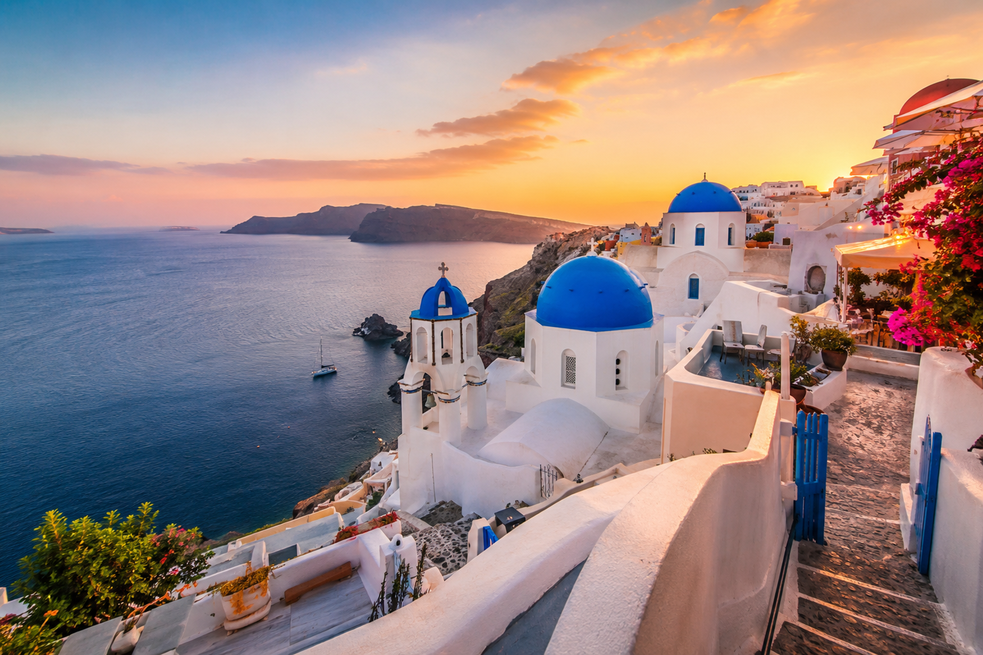 Santorini’s whitewashed cliffside buildings and blue-domed churches overlooking the Aegean Sea at sunset.