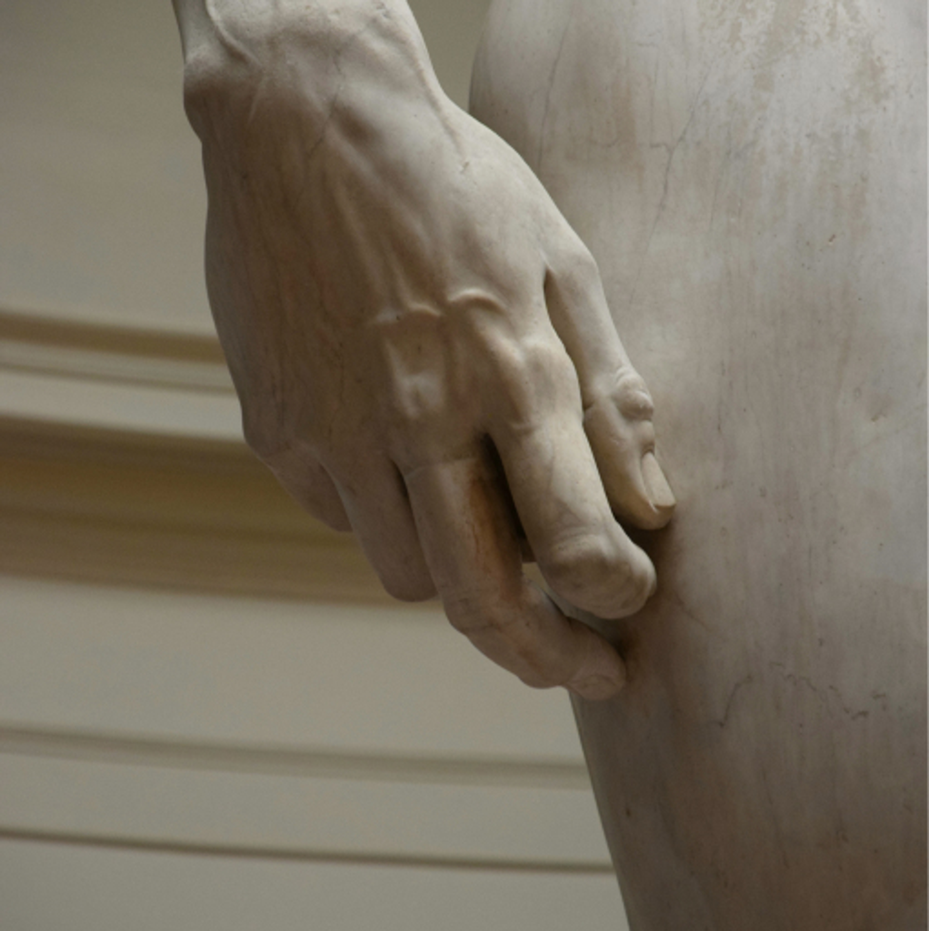 A close up of a carved marble statue's hand and thigh.