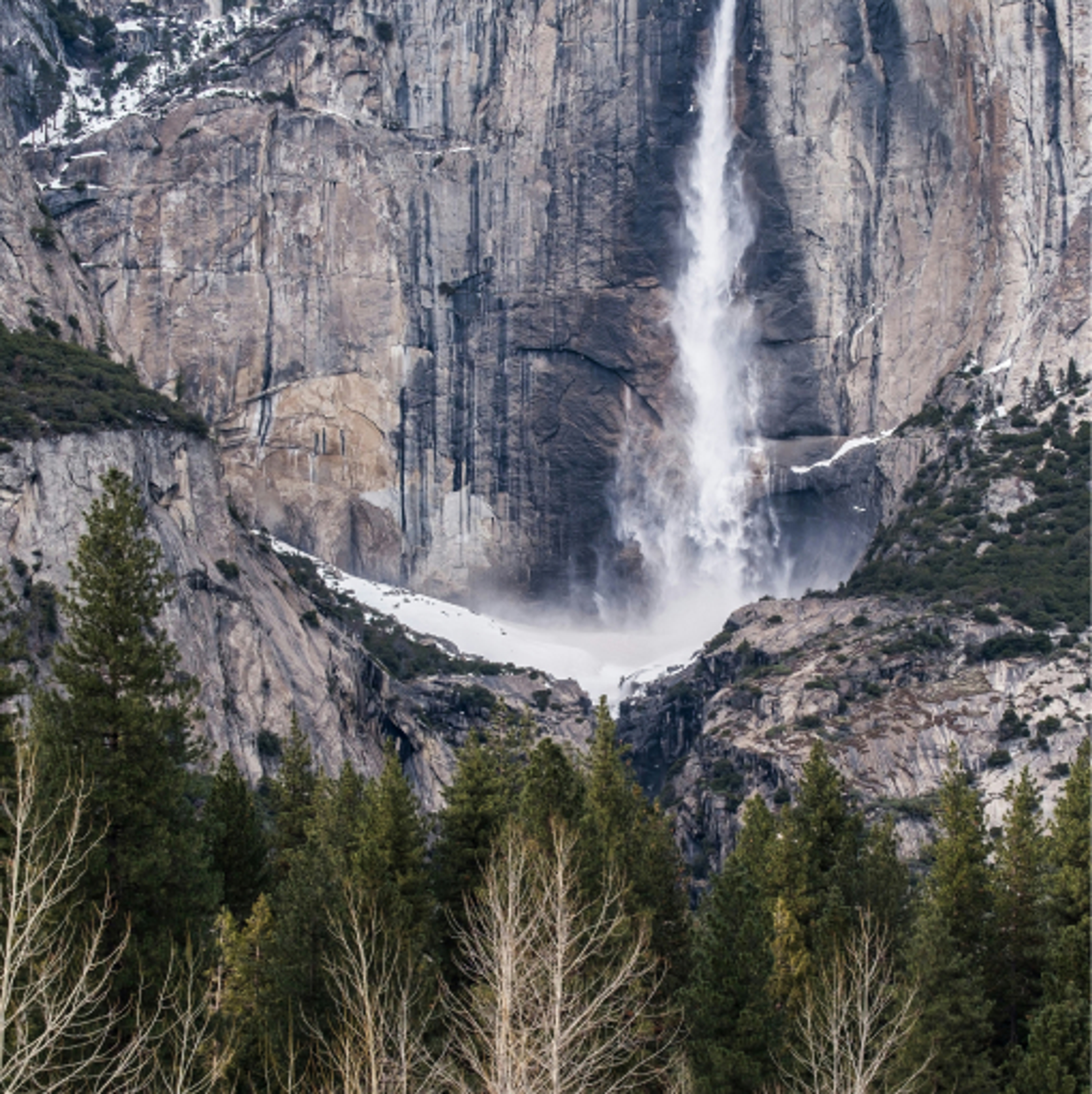 A quartz stone, granite textured mountain with a rushing waterfall amidst pine trees and greenery.