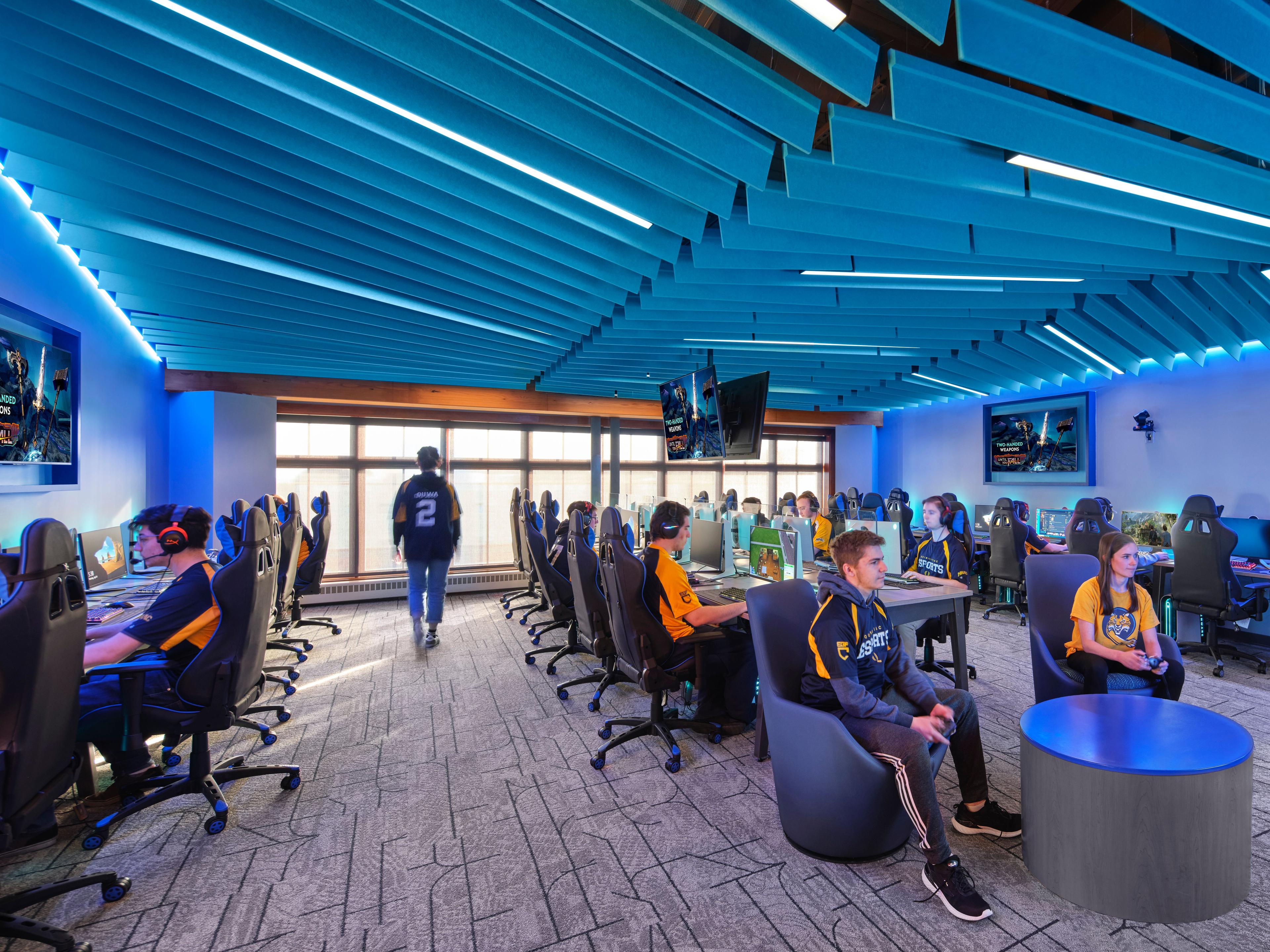 Angled blue baffles hang from the ceiling over students in an e-gaming center at a school.