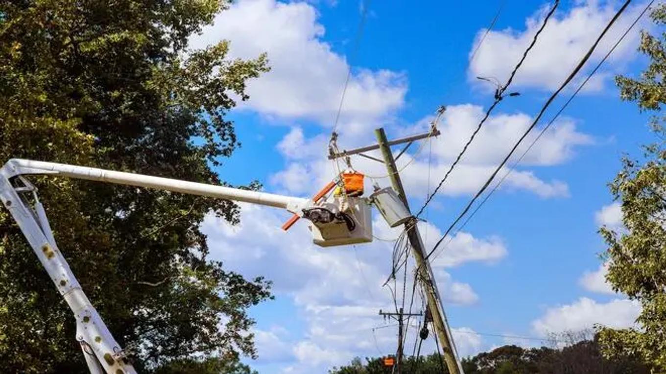 Utility worker in bucket lift repairing overhead power lines on a tilted utility pole outdoors