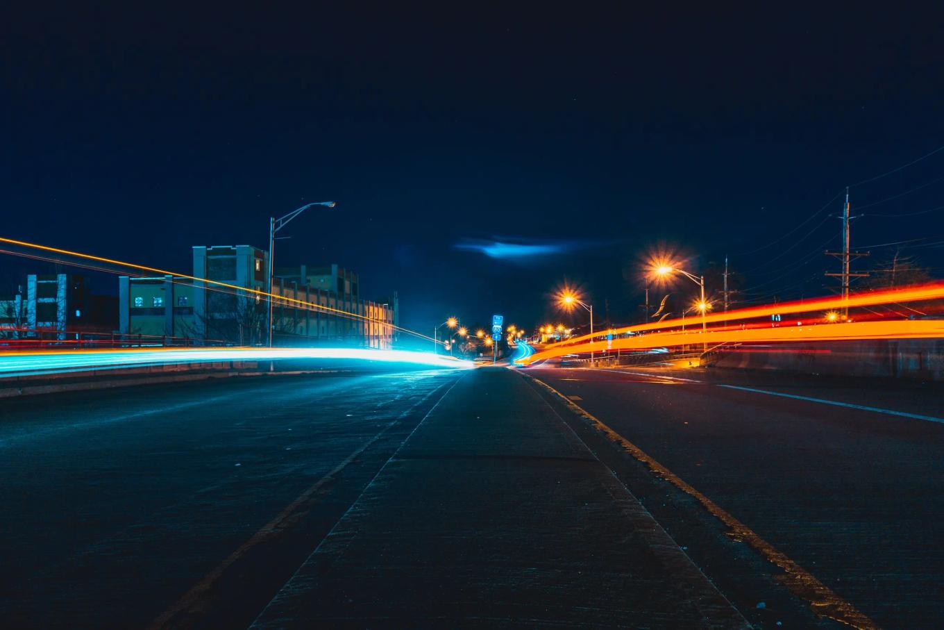 Long exposure view of vehicle light trails along an empty urban road at night with streetlights