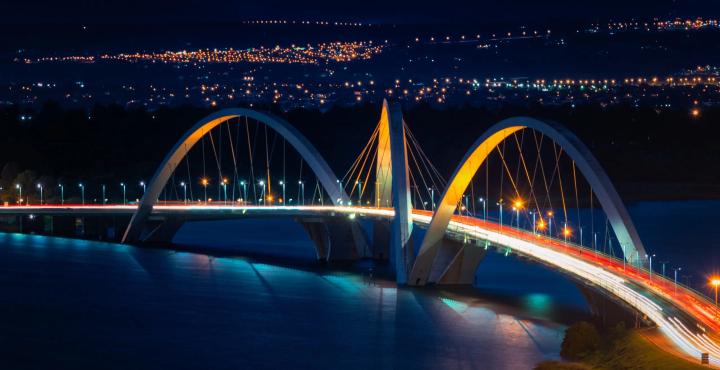 Arched bridge illuminated at night with vehicle light trails crossing over water