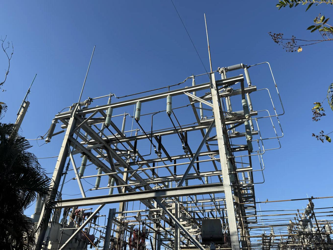 Electrical substation with metal structures, insulators, and fencing surrounded by trees
