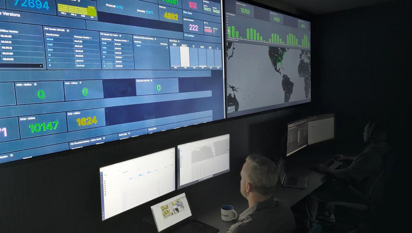 People seated at desks monitoring large wall screens displaying maps, charts, and system dashboards