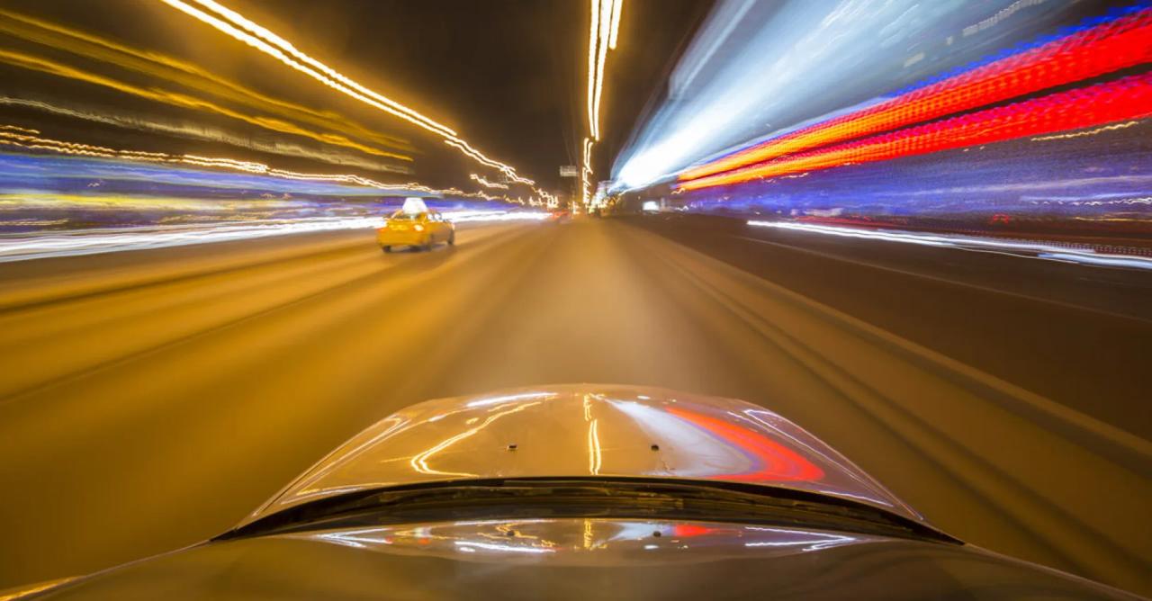 Forward view from a moving vehicle showing blurred city lights and traffic at night