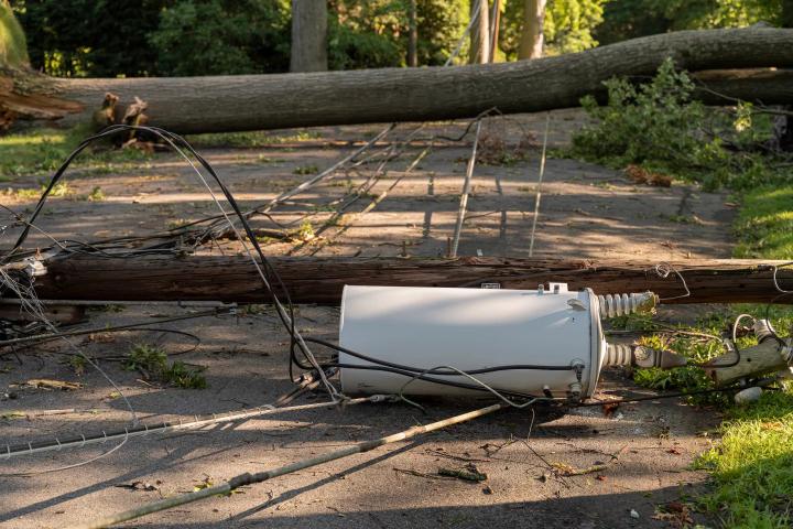Fallen utility pole with transformer and tangled power lines blocking a residential roadway