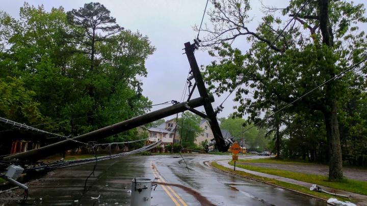 Broken utility pole with power lines collapsed across a wet residential roadway after a storm