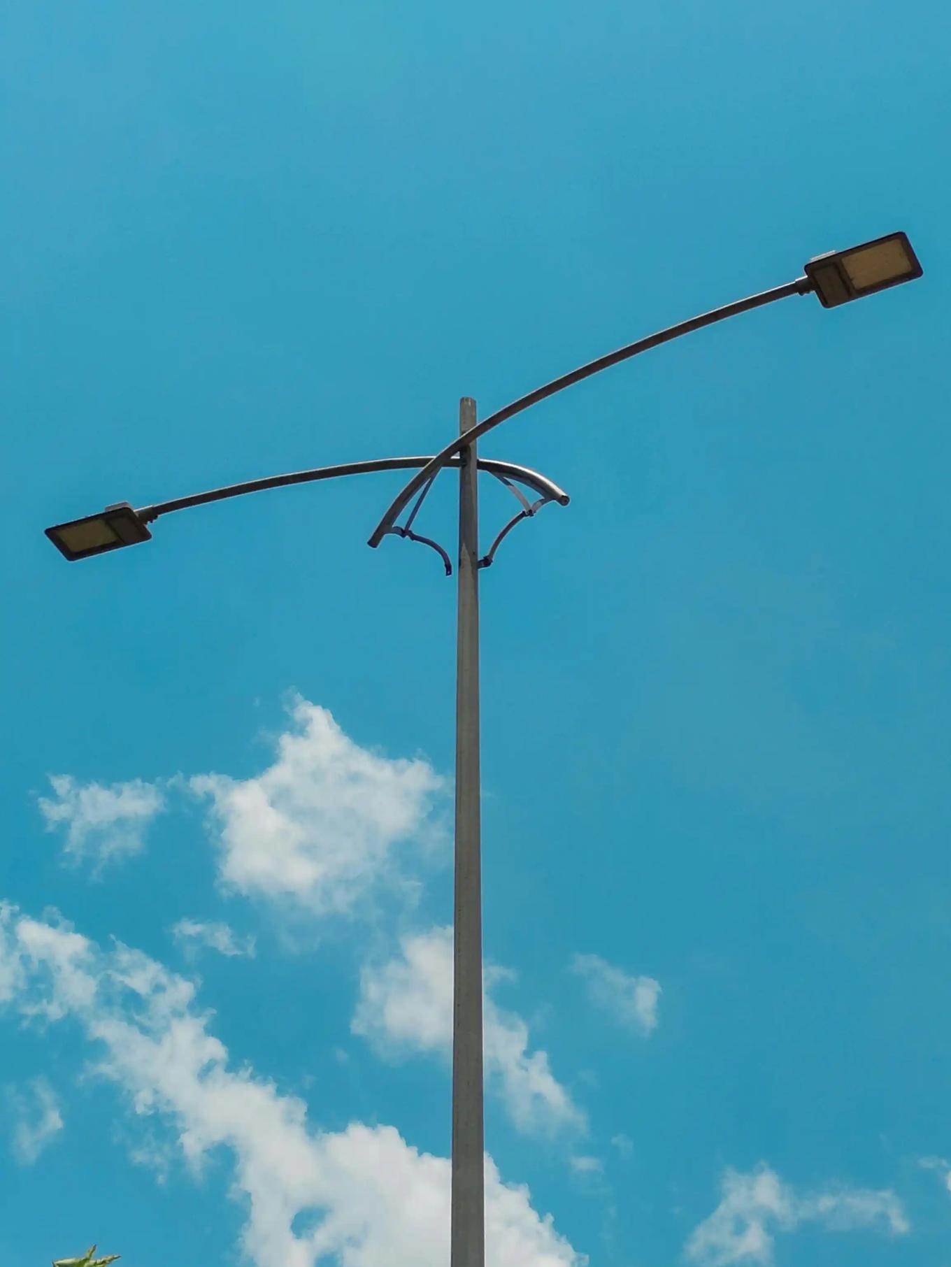 Tall streetlight pole with two curved light arms against a clear blue sky