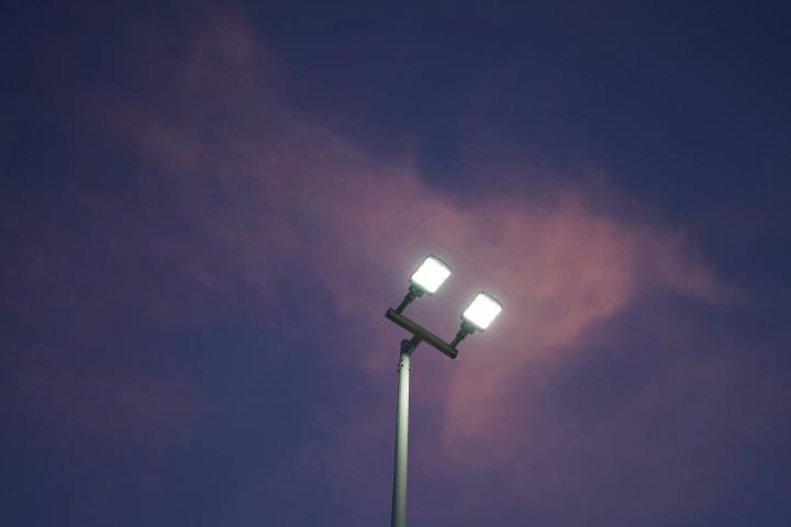 Two illuminated LED floodlights mounted on a tall pole against a purple evening sky with clouds