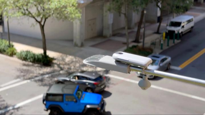 Streetlight-mounted UbiHub AI+ device attached to a pole overlooking an urban intersection with moving vehicles