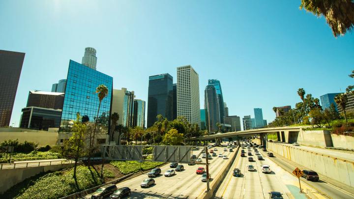 Multiple freeway overpasses carrying traffic through downtown Los Angeles with surrounding buildings and lighting poles