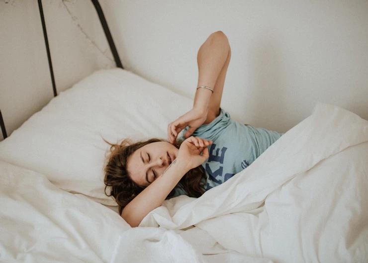A woman, eyes closed, stretches in bed.