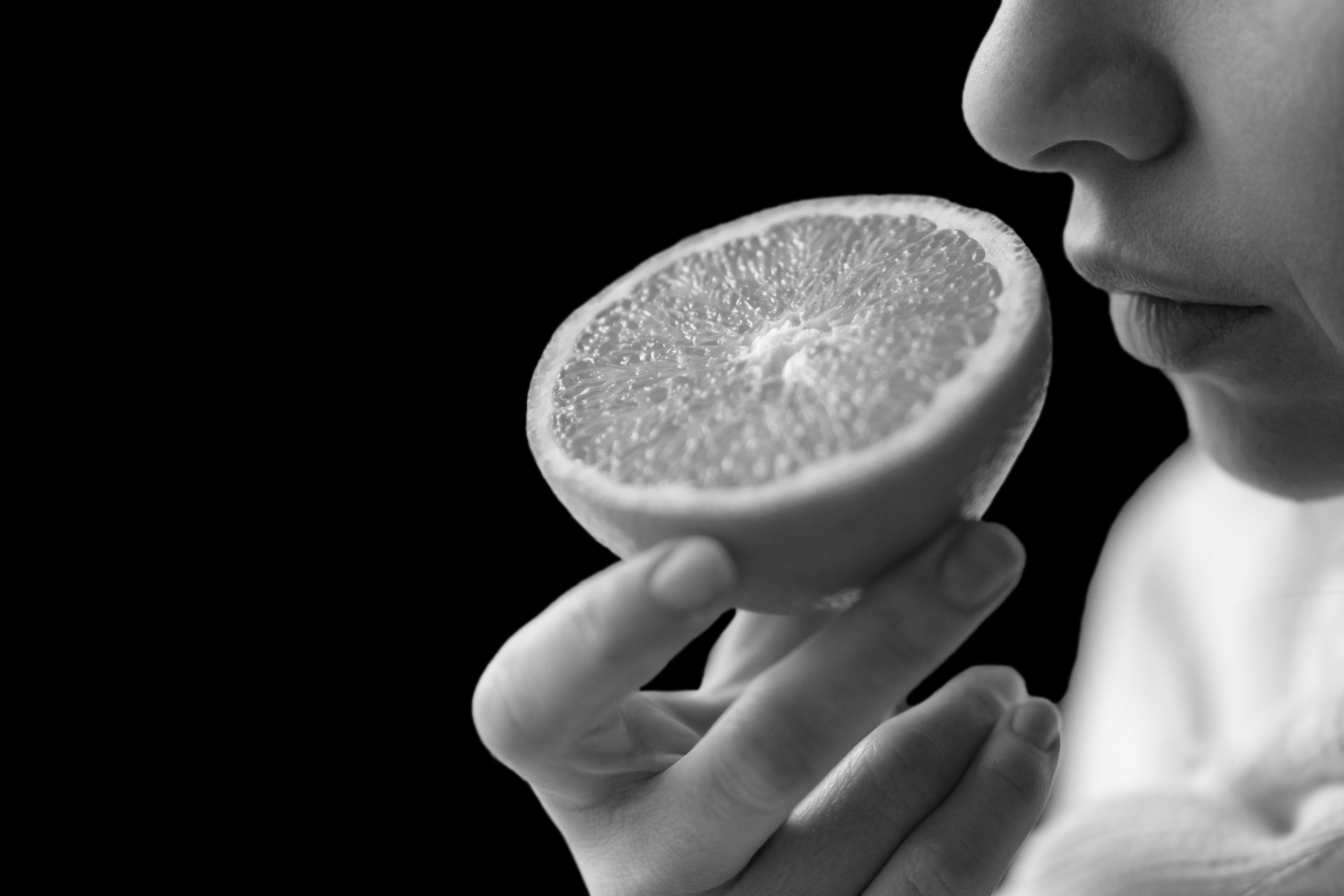 Black and white close up image of a woman smelling an orange