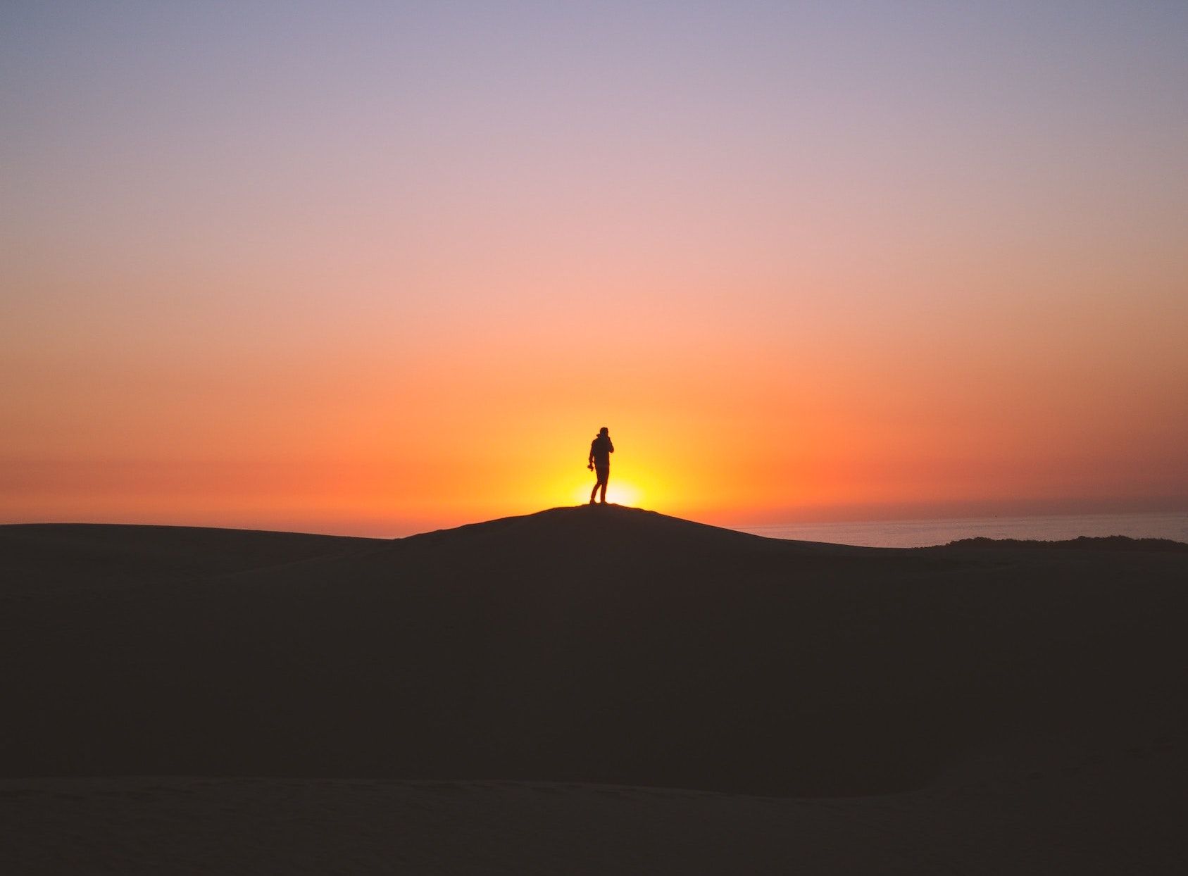 A person in shadow walks in front of a sunrise