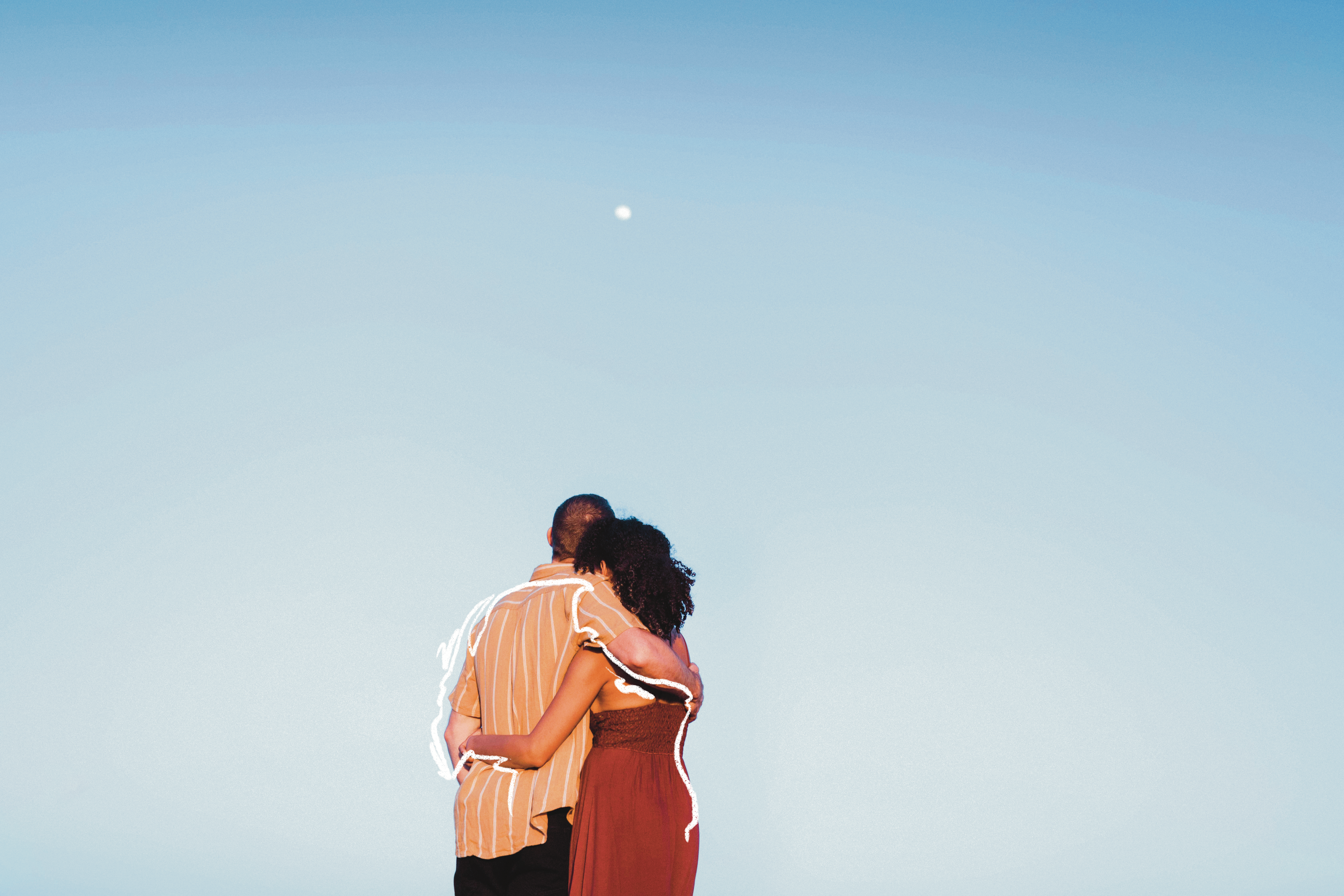 A man hugs a woman, shot from the back, and stare at the sky.