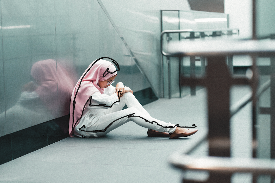 A woman sits alone in a stairwell with her head down.