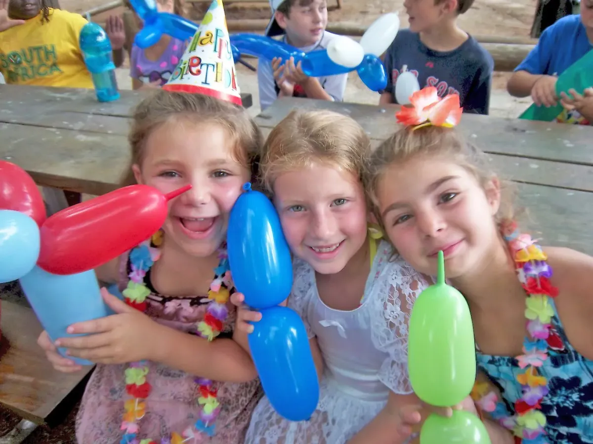 A group of young smiling girls standing next to each other at a birthday party.