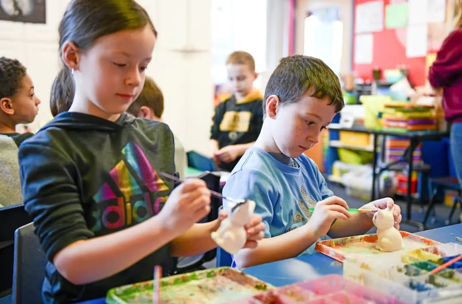 A group of young children sitting at a table painting ceramics