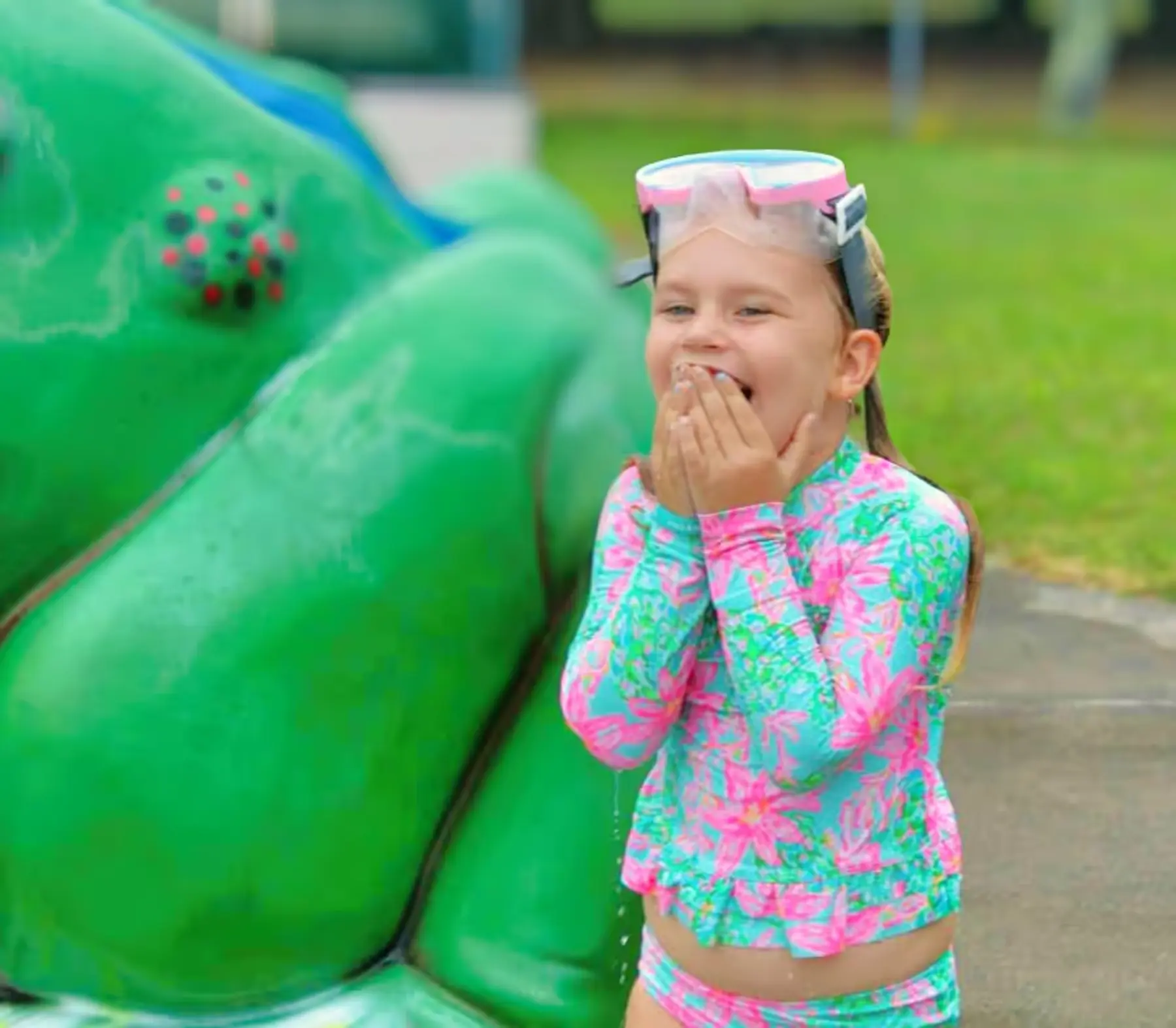 A little girl in a swim suit standing in front of a green frog statue