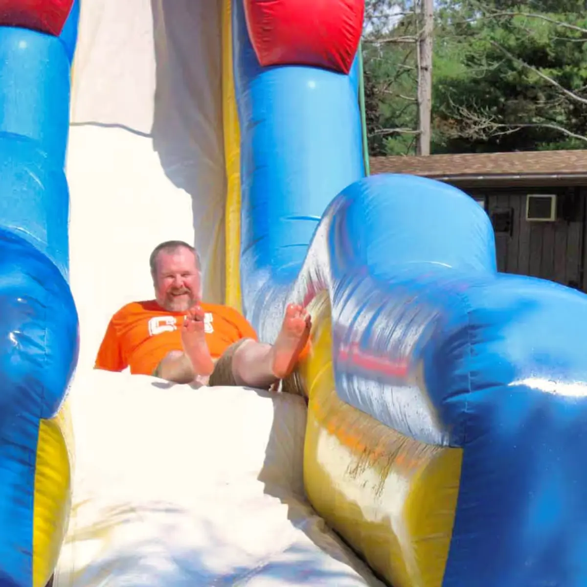 A middle-aged man standing on a huge inflatable slide with a big smile on his face
