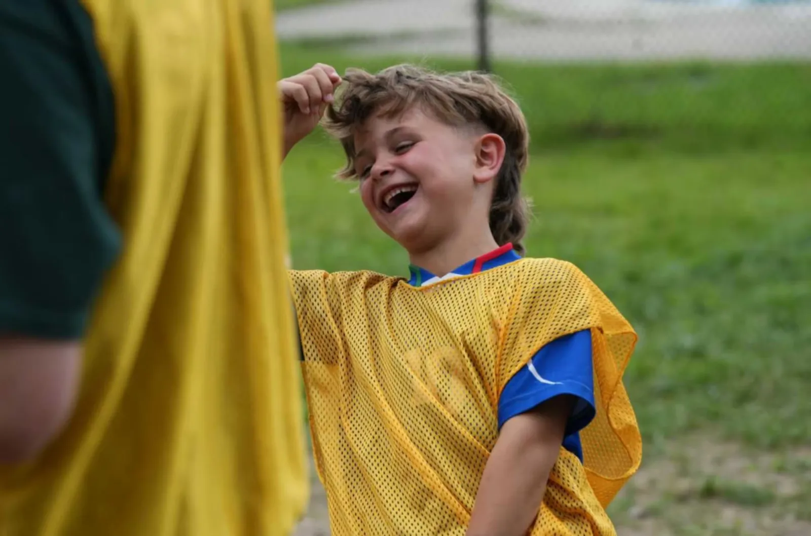 A laughing young boy in a yellow and blue soccer uniform