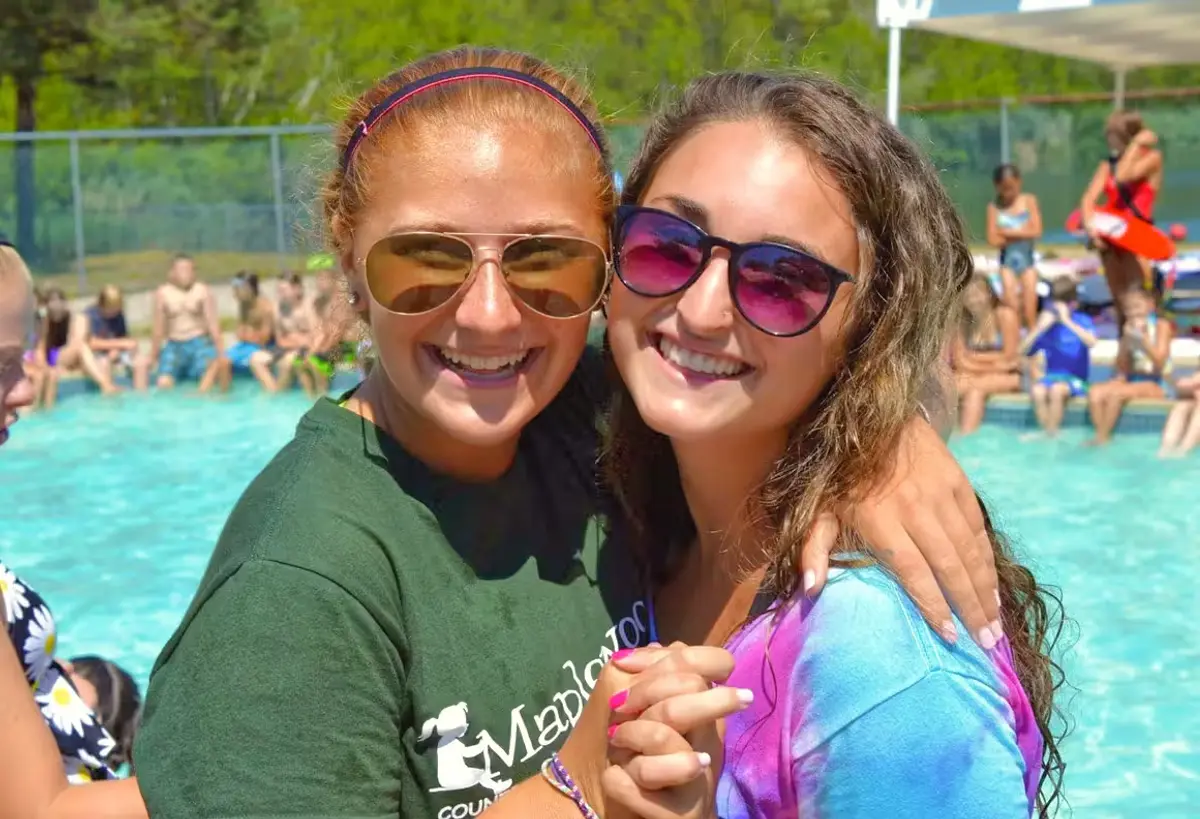 A couple of women standing next to each other near a pool
