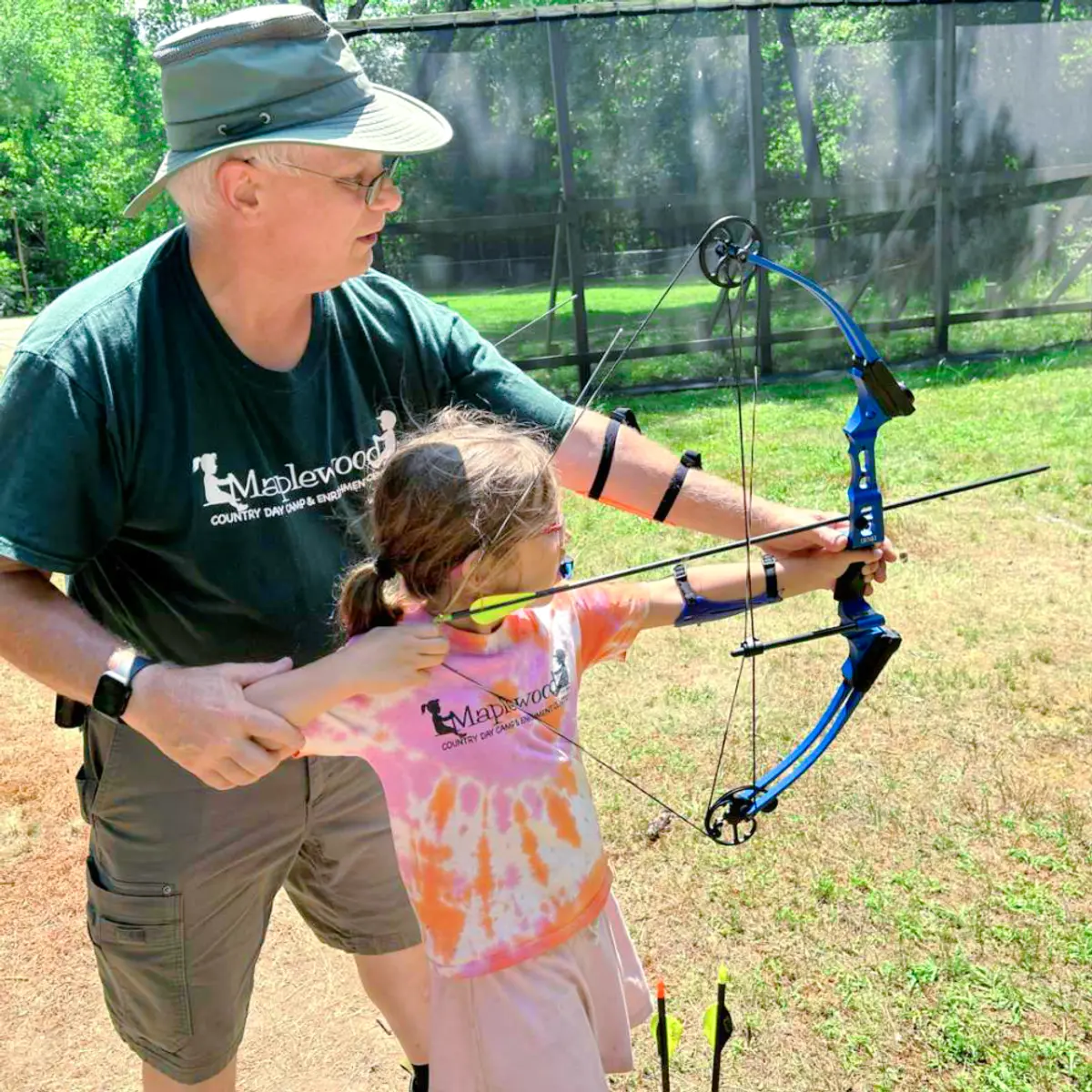 veteran maplewood staff teaching a little girl camper how to shoot a bow