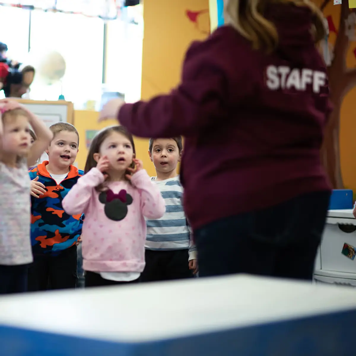A group of children standing around each other in front of a preschool teacher.