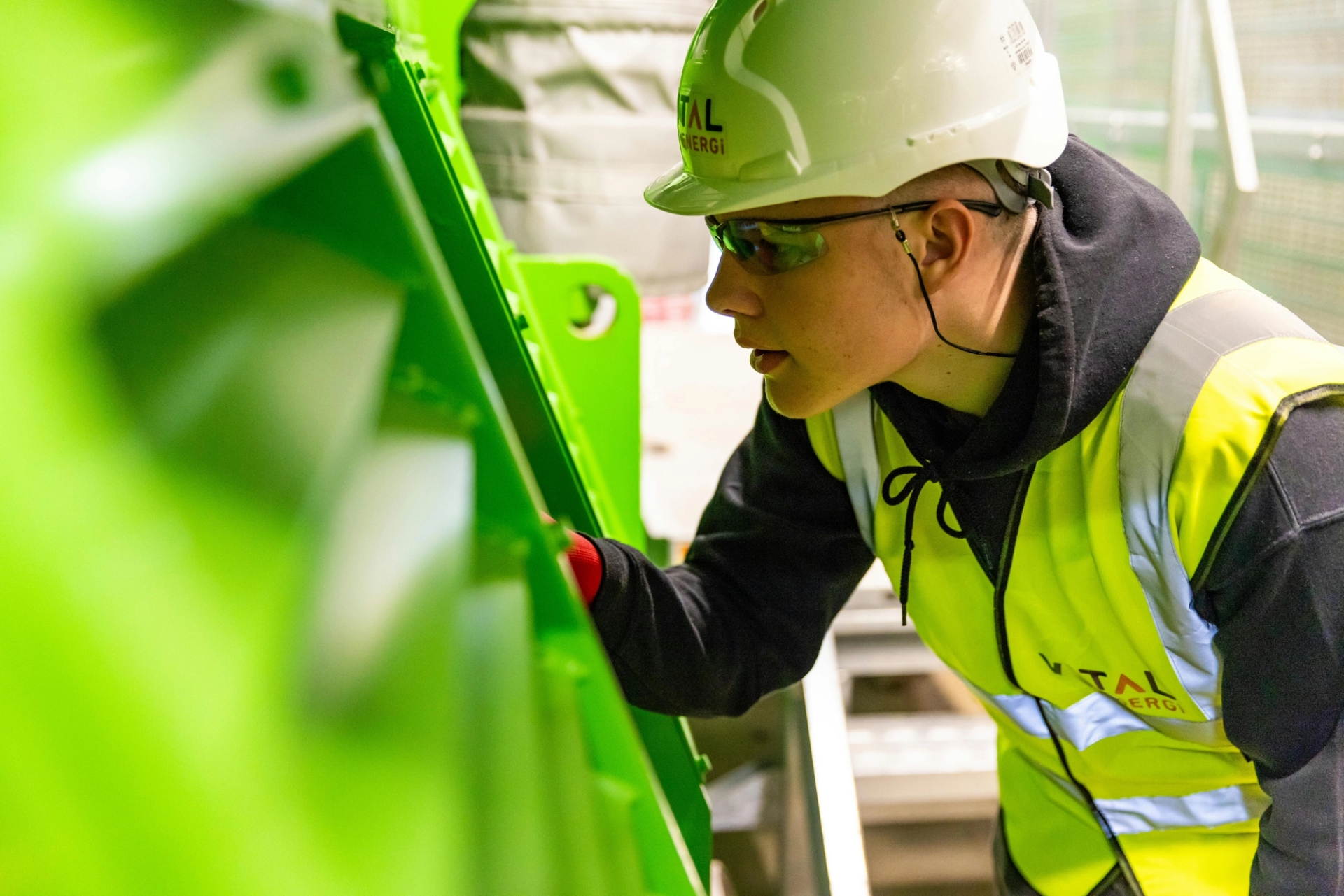 An engineer in safety gear inspects industrial machinery up close, representing the precision and quality control required in FAA-certified PMA parts manufacturing for aviation. 