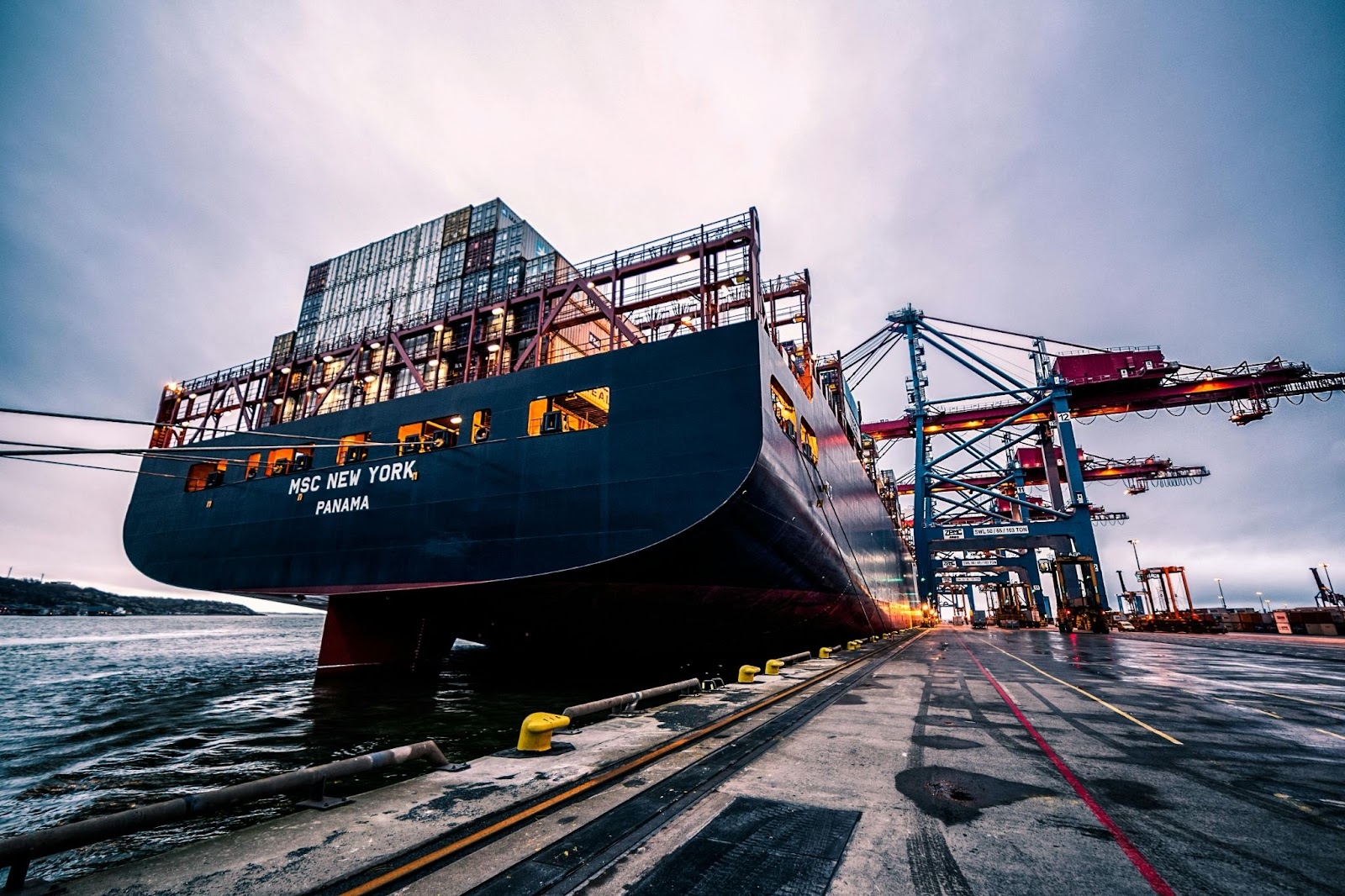 Een groot vrachtschip met het opschrift "MSC New York, Panama" meerde aan in een haven, met gestapelde containers en torenhoge kranen in beeld. Deze afbeelding illustreert de wereldwijde logistieke infrastructuur die cruciaal is voor de zichtbaarheid van de toeleveringsketen in de luchtvaart en efficiënt voorraadbeheer.